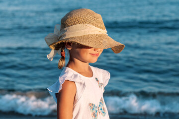 Sea Relax Summer holidays, vacation - beautiful little girl child wearing straw hat relaxing on beach near sea. Child in hat covering face from sun. Kid on sea lake background.