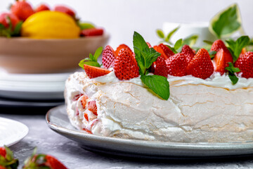 Meringue roll with strawberry filling and whipped cream. Summer dessert decorated with strawberries and mint on a gray background