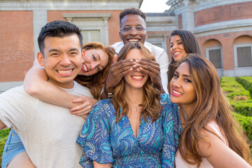 Obraz premium Man blocking friend's eyes while standing with a group of friends outdoors