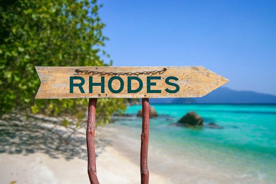 Rhodes wooden arrow road sign against beach with white sand and turquoise water background. Travel to Greece concept.
