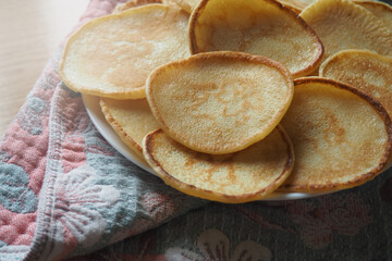 Pancakes on a wooden table in a white bowl with a towel. Breakfast and cooking with flour.