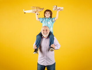 Child boy and grandfather playing piggyback ride with plane and wooden toy truck. Men generation granddad and grandchild. Elderly old relative with child.