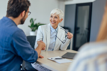A smiling female insurance agent finished the meeting, shaking hands with a male client.