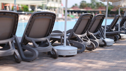 Many empty sun loungers and parasols standing near swimming pool