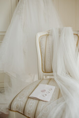 Wedding rings on a wedding invitation card on a white chair in a bright room against the backdrop of the bride's white dress