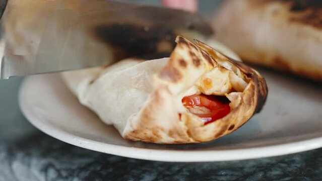 Cooking, I cut fried shawarma in the plate. Close-up in motion. Black stone countertop.