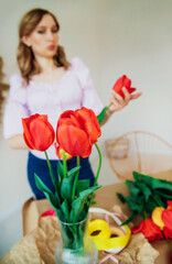 A young woman is packing a festive bouquet in wrapping paper. The florist makes an assembly with red tulips in the workshop. A woman at work, in a small business or hobby.