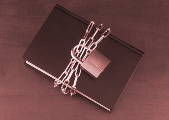Banned information and security concept, book with chain and padlock on wooden table.