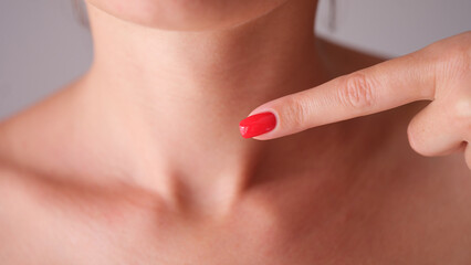 Woman with red manicure pointing finger at neck area with thyroid gland closeup