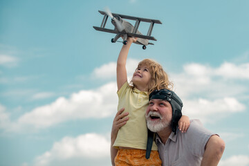 Old grandfather and young child grandson playing with toy airplane against summer sky background....