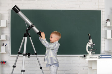 Cute little child with telescope in classroom at elementary school. - obrazy, fototapety, plakaty
