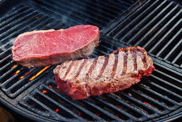 Raw dry aged wagyu roast beef steak grilled as close-up on a charcoal grill with fire and smoke