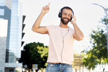 Portrait of happy hispanic man wearing headphones listening music on the street. Smiling bearded...