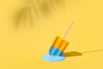 Colored yellow and blue ice cream melts from the hot sun. Palm leaves shadow. Hot weather concept