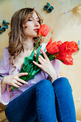 A young woman is holding a bouquet of red tulips and sitting on a wooden podium. The concept of March 8, Valentine's Day. A wonderful gift for a girl. Spring portrait of a woman.