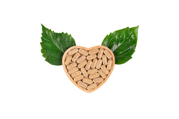 Herbal pills in heart shaped wooden plate and green leafs in the form of wings on blue background.