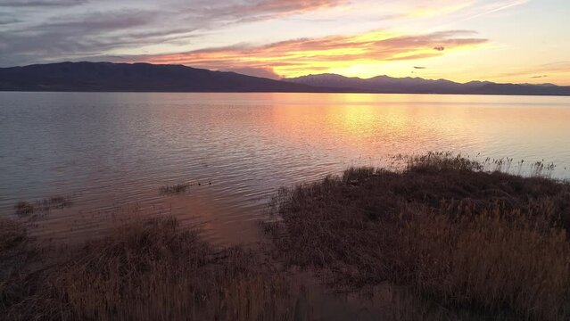 Panning along lake looking at colorful sunset overlooking Utah Lake as the sky reflects in the water.