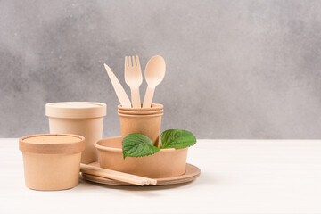Catering, paper utensils - paper plates, food containers, cups and wooden cutlery set against gray wall background with copy space. Sustainable food packaging concept
