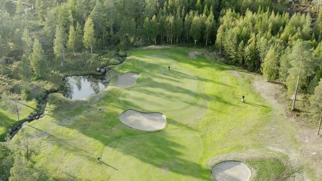 Cinematic aerial footage over colorful green golf course - few unidentified people play golf. Vibrant colors, drone footage.