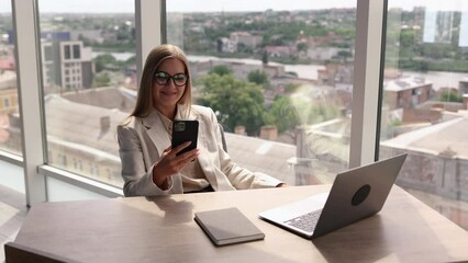 Smiling young business woman professional talking on phone using laptop sit at home office desk, happy female customer make mobile call confirming online website shopping order delivery concept