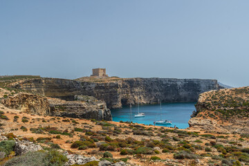 The small island of Comino with yachts on the Crystal Lagoon overlooked by the small watchtower called Saint Mary's Tower built in 1618.
