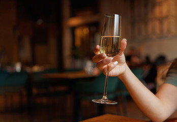 Female hand with french manicure holding a glass with wine or champagne on naturally blurred background. Woman in restaraunt, cafe. Luxury pasttime, celebration concept. 