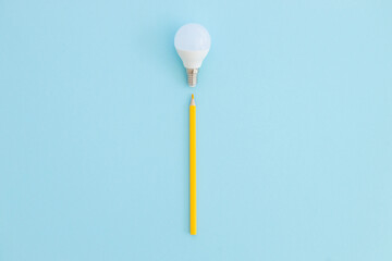 LED lamp and pencil lies on a pastel blue background. Nearby - pieces of satin yellow ribbon symbolize the rays of light from the lamp. Idea concept.