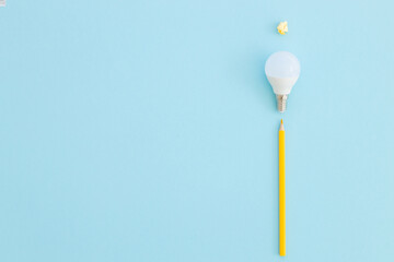 LED lamp and pencil lies on a pastel blue background. Nearby - pieces of satin yellow ribbon symbolize the rays of light from the lamp. Idea concept.