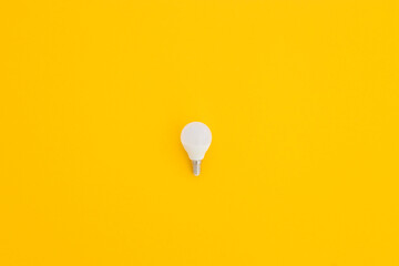 LED light bulb lies on a pastel yellow background. Energy saving concept. Minimalism, top view