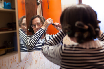 Obraz na płótnie Canvas Senior Woman Comb Her Hairs in the Mirror of Home Bathroom