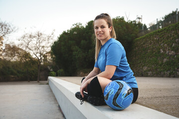 Content female soccer player with ball sitting on border in park - Powered by Adobe
