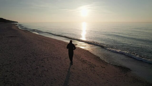 A runner, at sunset, he runs along the beach along the waves.