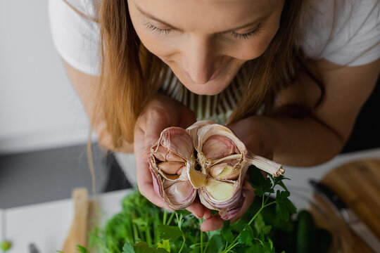 Closeup smiling woman face hold, smell head of garlic on table in kitchen. Healthy eating. Natural antibiotic untivirus 