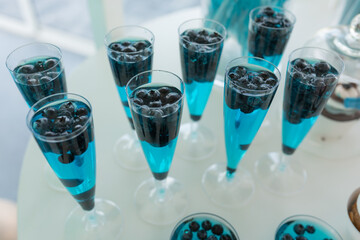 Serving row of glasses of refreshing colorful drinks with blueberry closeup, white background. Pouring sparkling wine into glasses, event celebration. Banquet hall, festive party, luxurious service