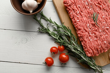 Fresh raw meat or ground chicken meat on a wooden cutting board with thyme, spices and garlic. White wooden background. Top view. Copy space.