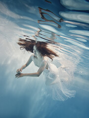 A girl in a dress with lace swims underwater as if in zero gravity