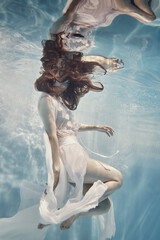 A girl in a dress with lace swims underwater as if in zero gravity