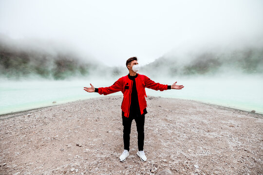 young man in red bomber jacket standing at kawah putih sulfer lake in Bandung