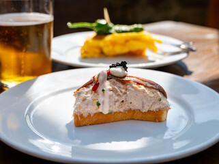 Sunny day in San Sebastián, typical food and drink in bars of Basque Country, pinchos or pinxtos, small slices of bread with different toppings and glass of beer, lunch in Spain