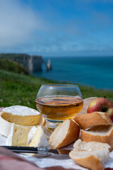 Lunch on green grass fields on chalk cliffs of Etretat, french cheese camembert and apple cider drink with Atlantic ocean on background, Normandy, France