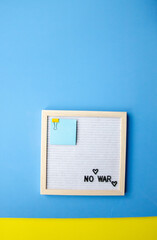 Flatlay vertical composition with a blue background, a letter board in a wooden frame with the phrase NO WAR and blue  sticker