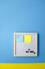 vertical composition with a blue background, a letter board in a wooden frame with the phrase NO WAR and blue yellow stickers