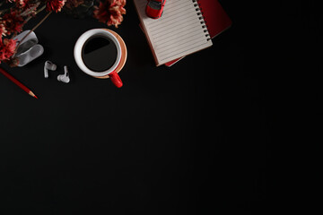 Naklejka premium Top view cup of coffee, blank notepad, earphone and flower pot on black background. Copy space