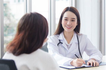 Asian professional doctor woman who wears medical coat talks with woman patient to suggest treatment guideline and healthcare concept in office of hospital.