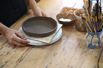 Close up view mature woman decorating and shaping pottery before baking in workshop. Indoors lifestyle activity, handicraft, hobbies concept