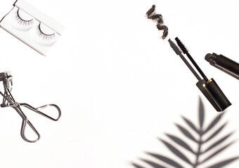 Black mascara frame with brush smear, eyelash curler and false eyelashes on the bright white background. Cosmetic isolated products. Copy space