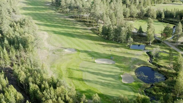 Cinematic aerial footage over colorful green golf course - few unidentified people play golf. Vibrant colors, drone footage.