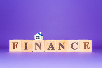 FINANCE word written on wood blocks,miniature toy house and number cubes put on purple ,veri peri background.Copy space.