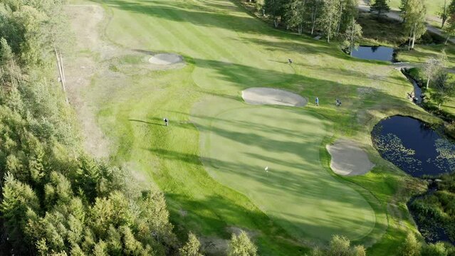 Cinematic aerial footage over colorful green golf course - few unidentified people play golf. Vibrant colors, drone footage.