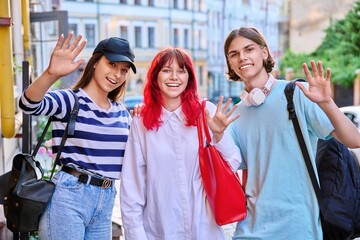 Group of teenage friends looking at camera waving hand, outdoor